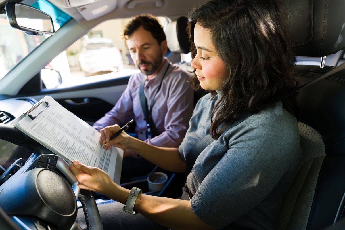 Female student with driving instructor reviewing a checklist in vehicle